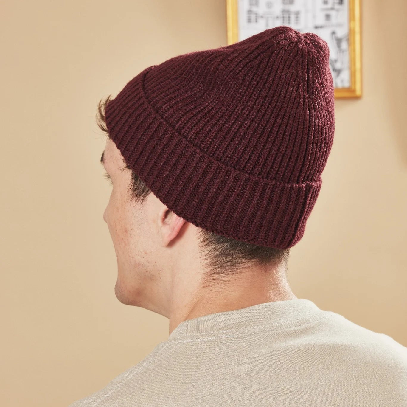 Person wearing a burgundy knit beanie against a beige wall.