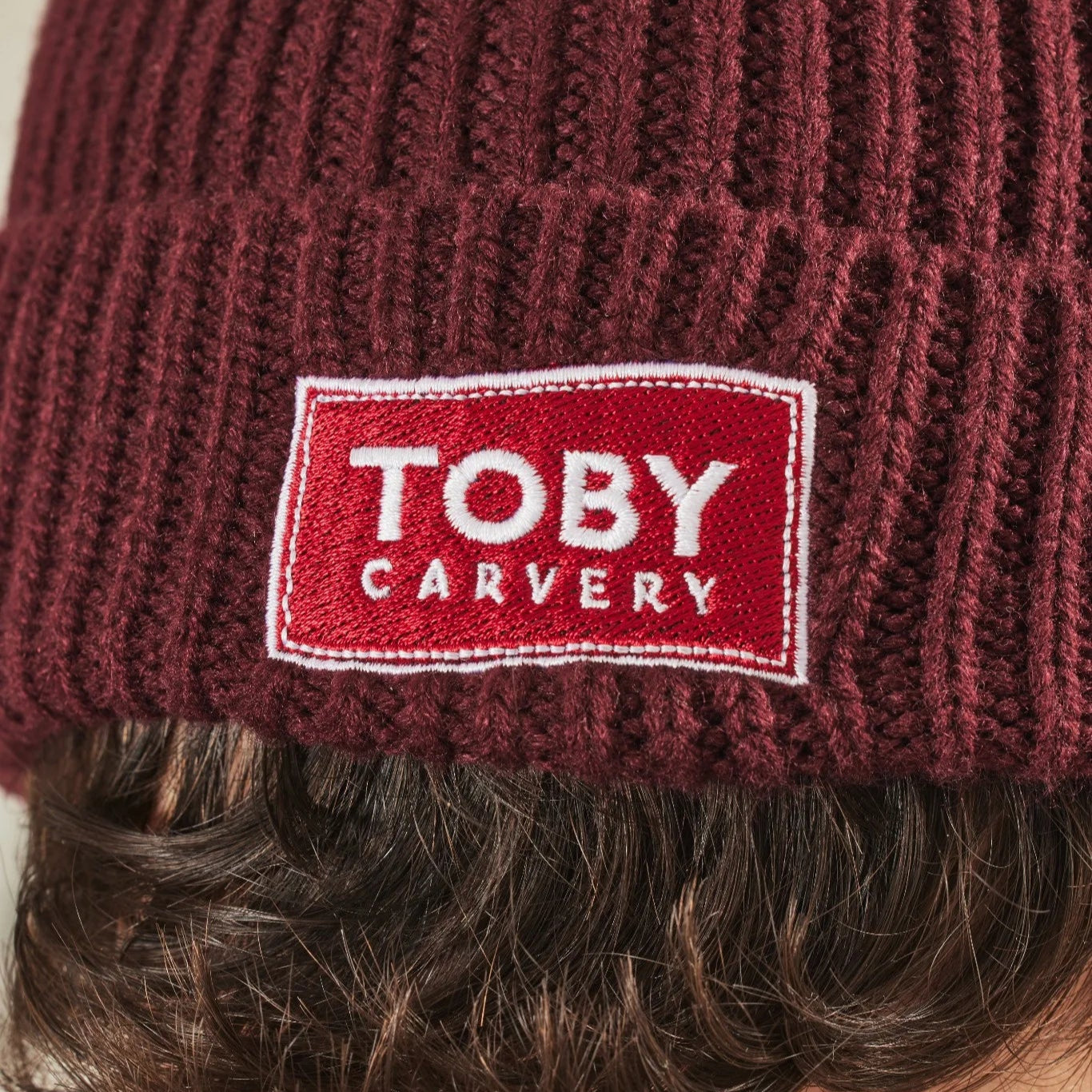 Close-up of a burgundy knit beanie with a red 'Toby Carvery' label.