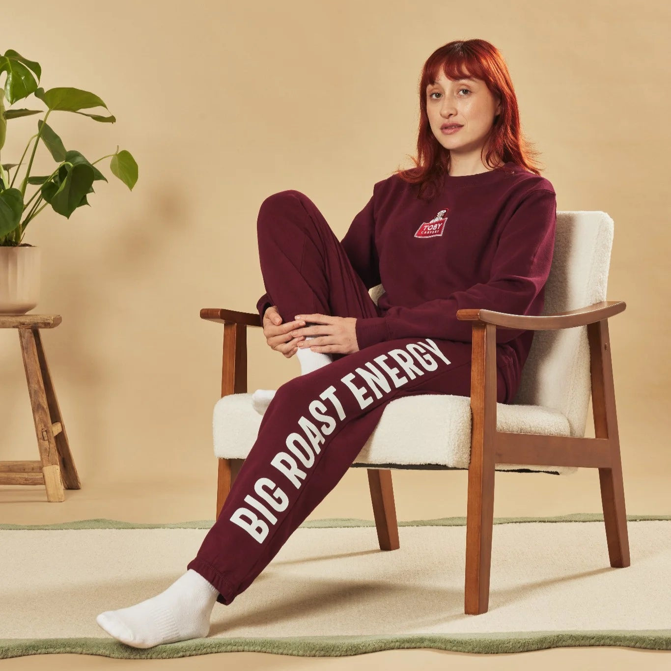 Person wearing a burgundy tracksuit with 'Big Roast Energy' text, sitting in a chair.