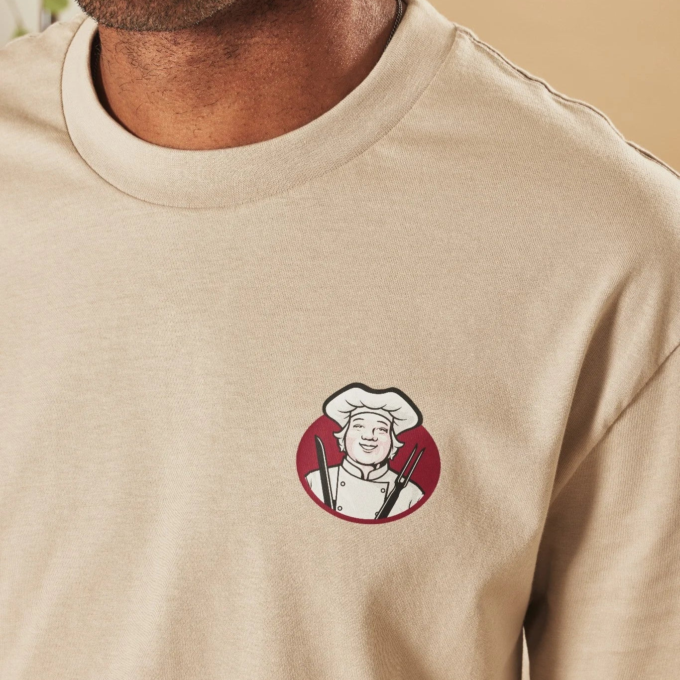 Man wearing a natural stone t-shirt with a Toby Carvery logo on the chest against a beige background