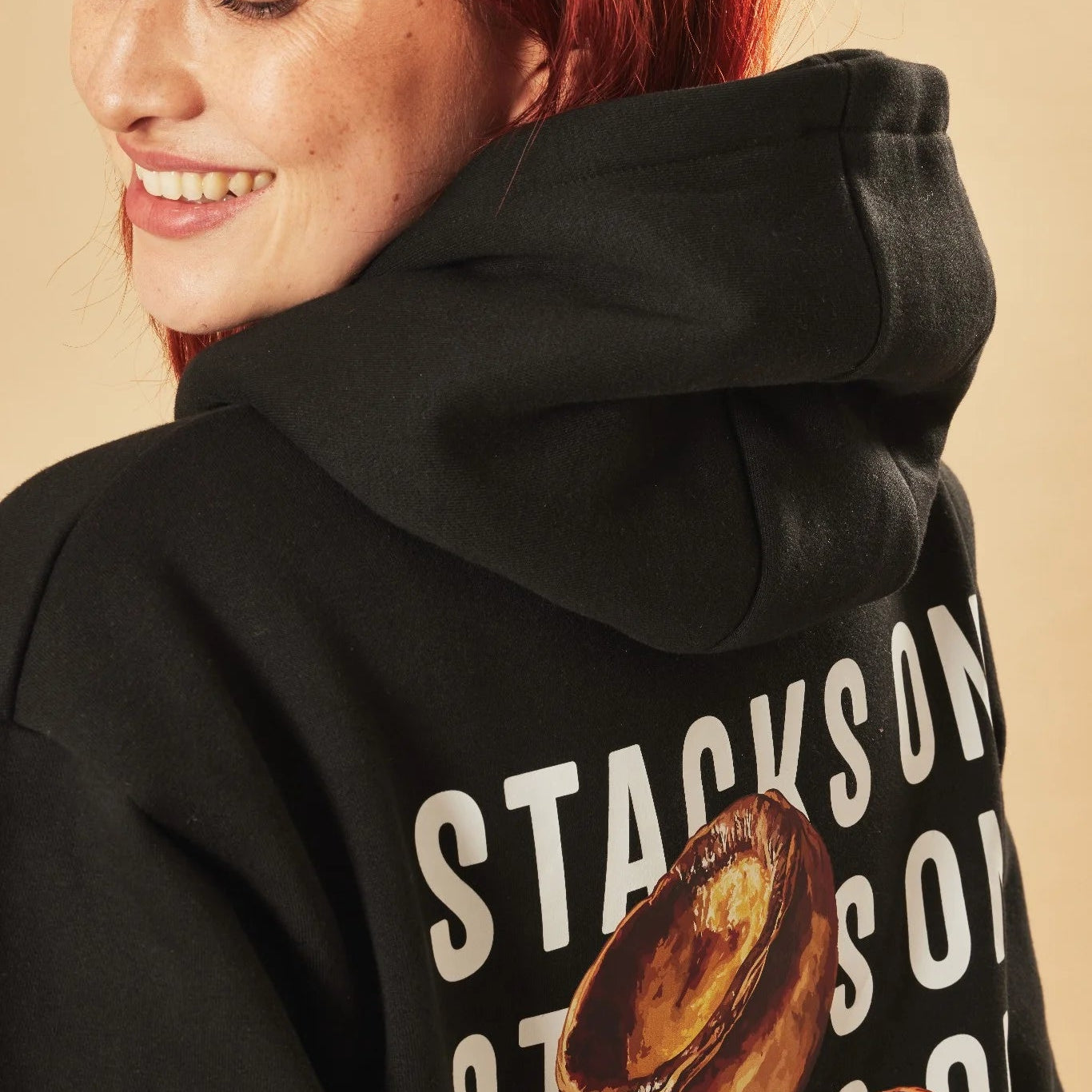 Person wearing a black hoodie with 'Stacks on' text on the back against a beige background