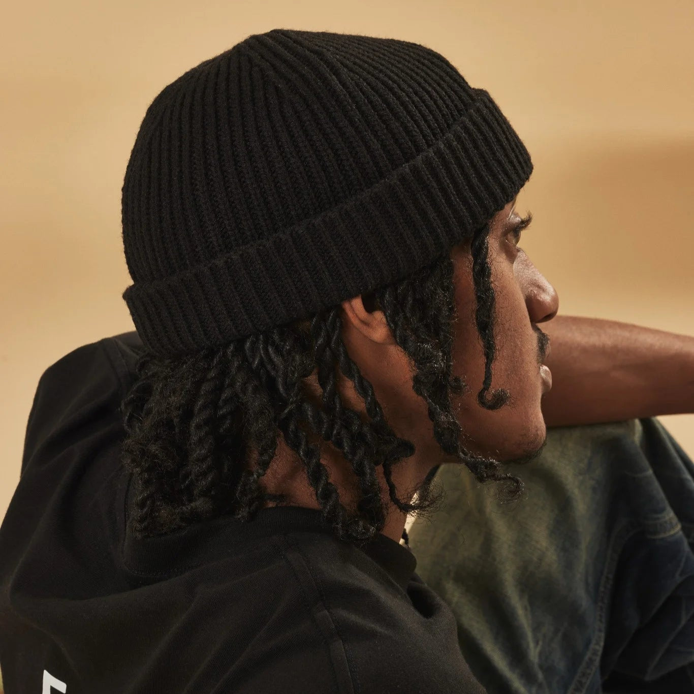 Person wearing a black knit beanie against a beige background