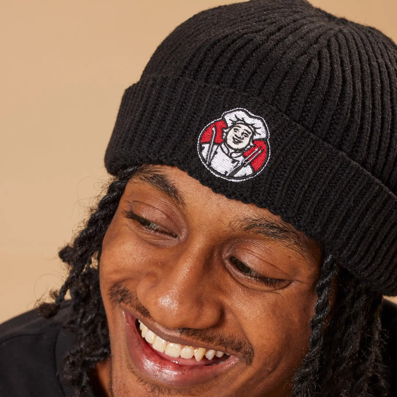 Person wearing a black beanie with a Toby Carvery logo on a beige background