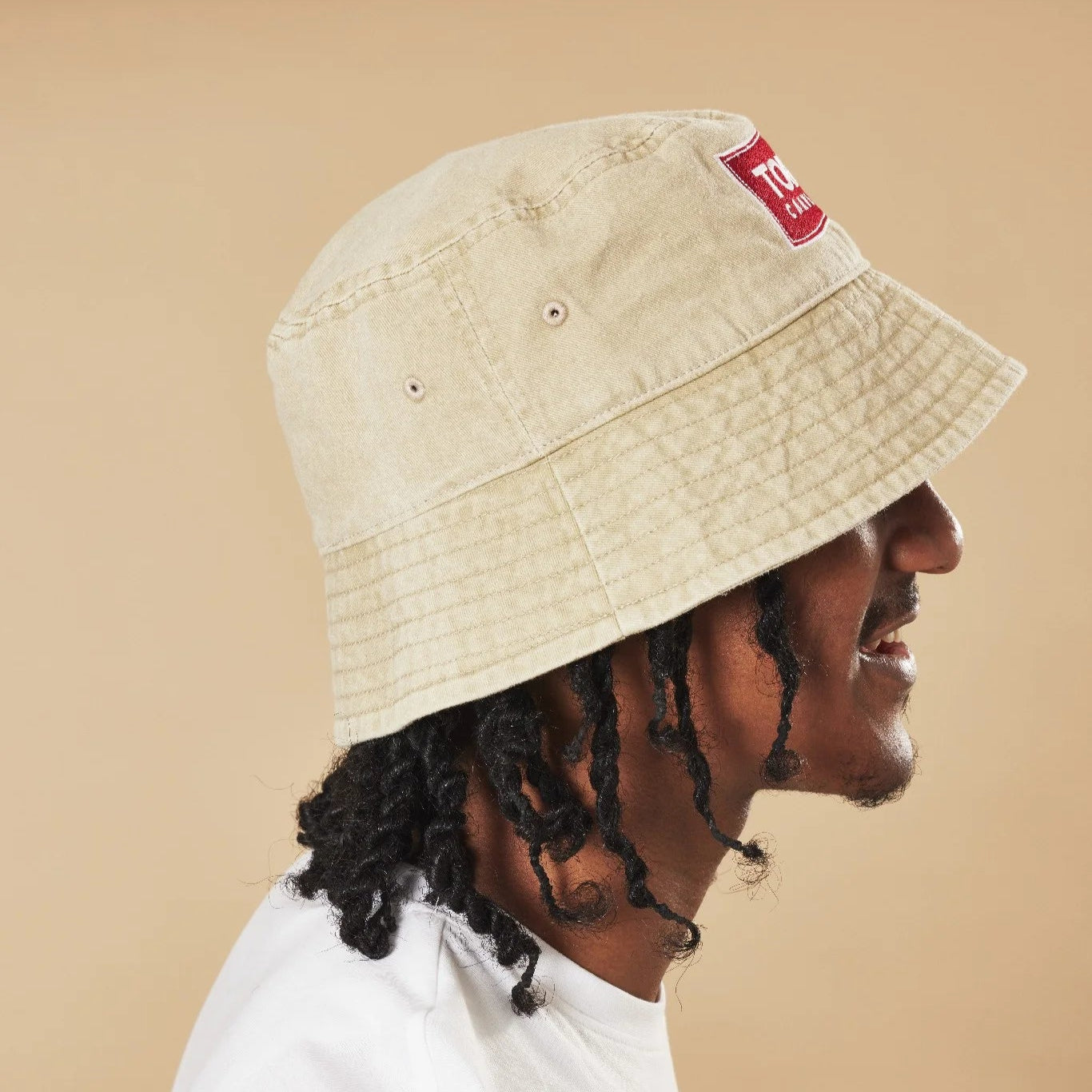 Person wearing an oatmeal bucket hat with a red label on a beige background