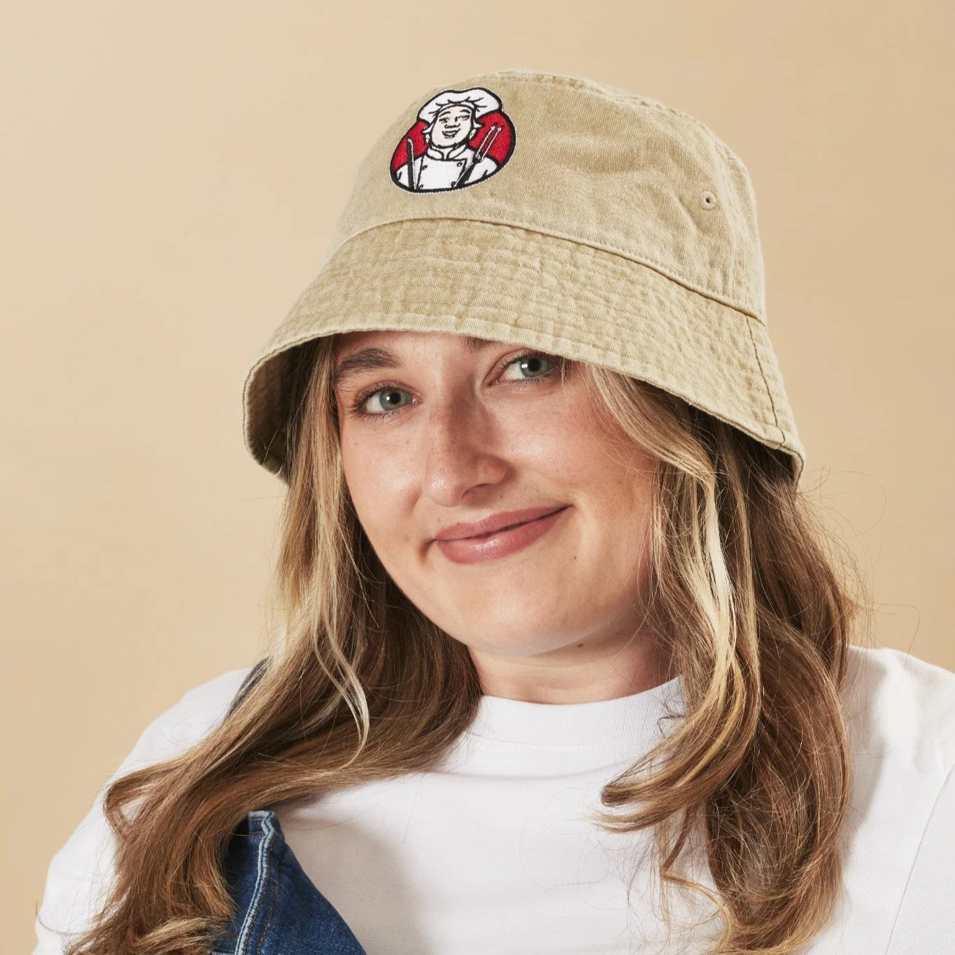 Person wearing an oatmeal bucket hat with a logo on a beige background