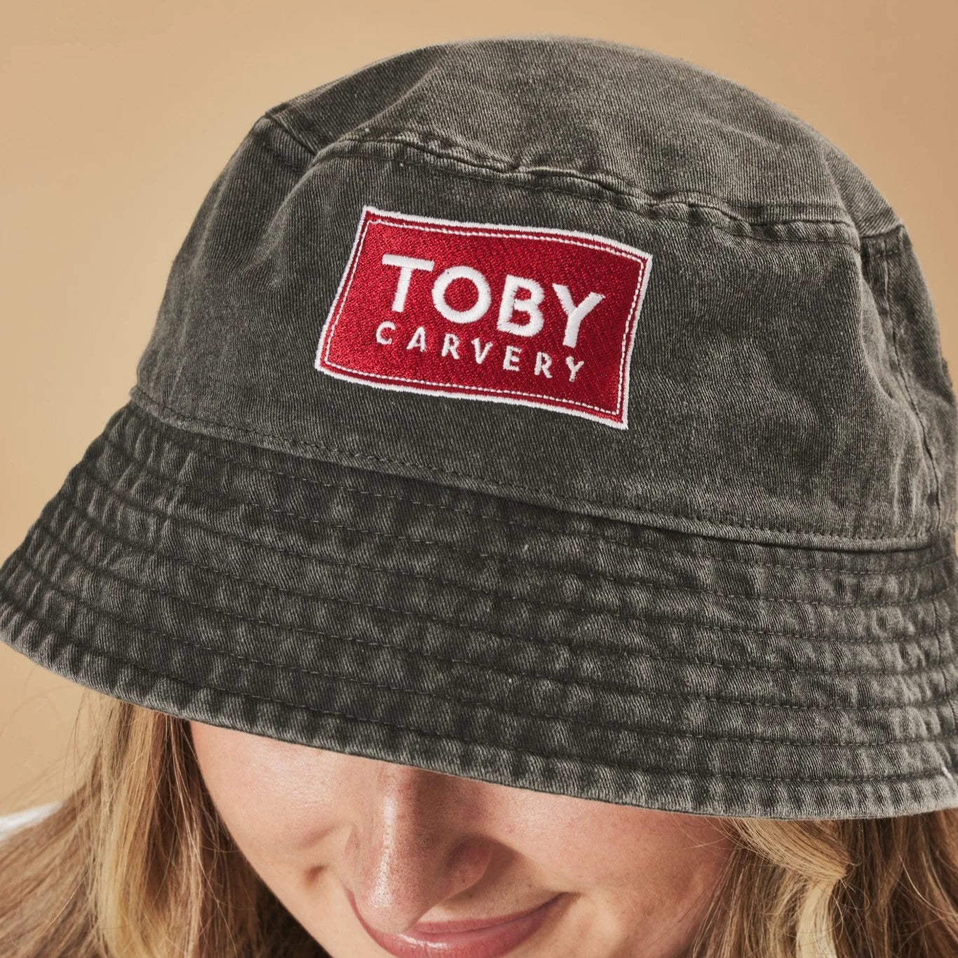 Graphite bucket hat with a red and white 'Toby Carvery' logo on a beige background