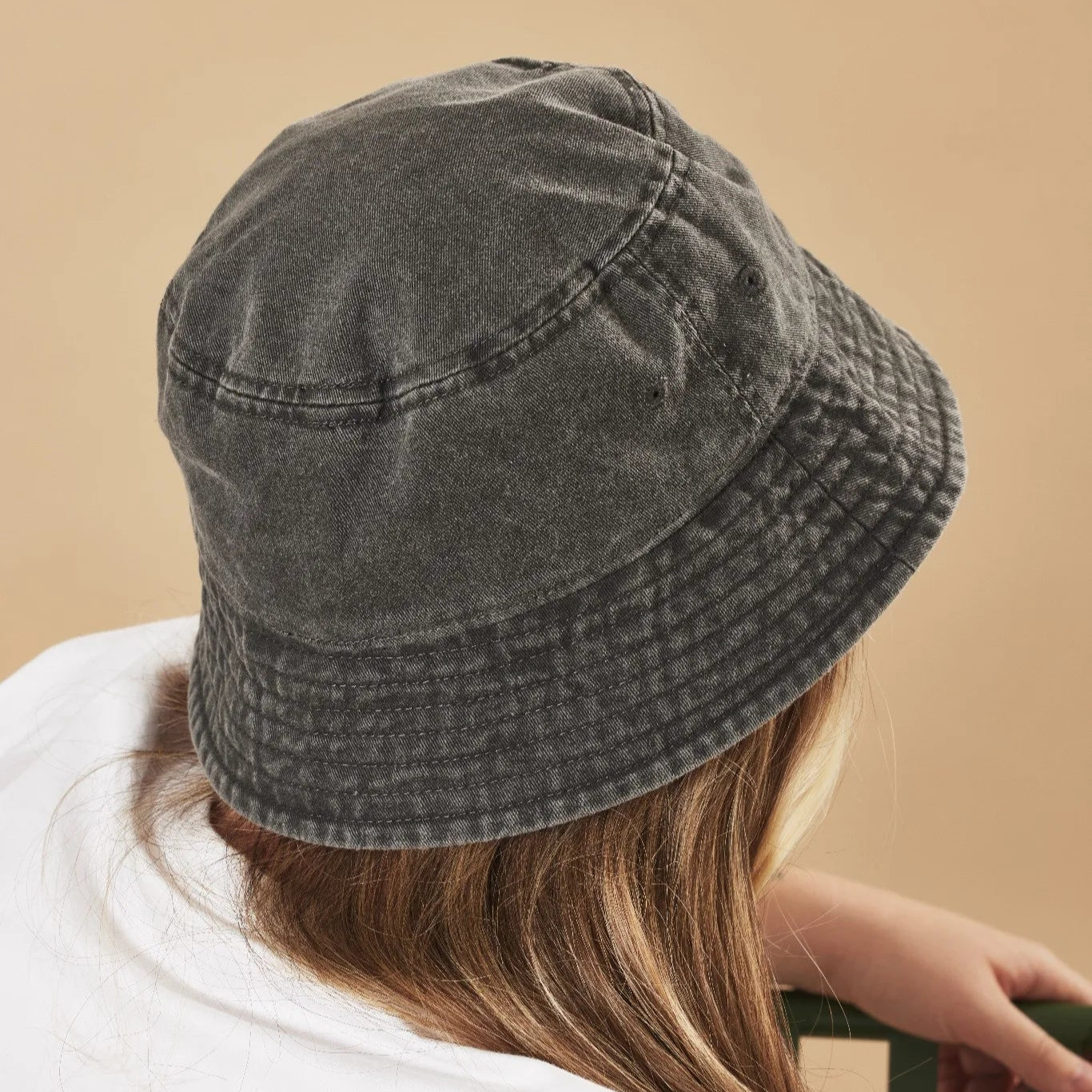 Person wearing a graphite bucket hat against a beige background