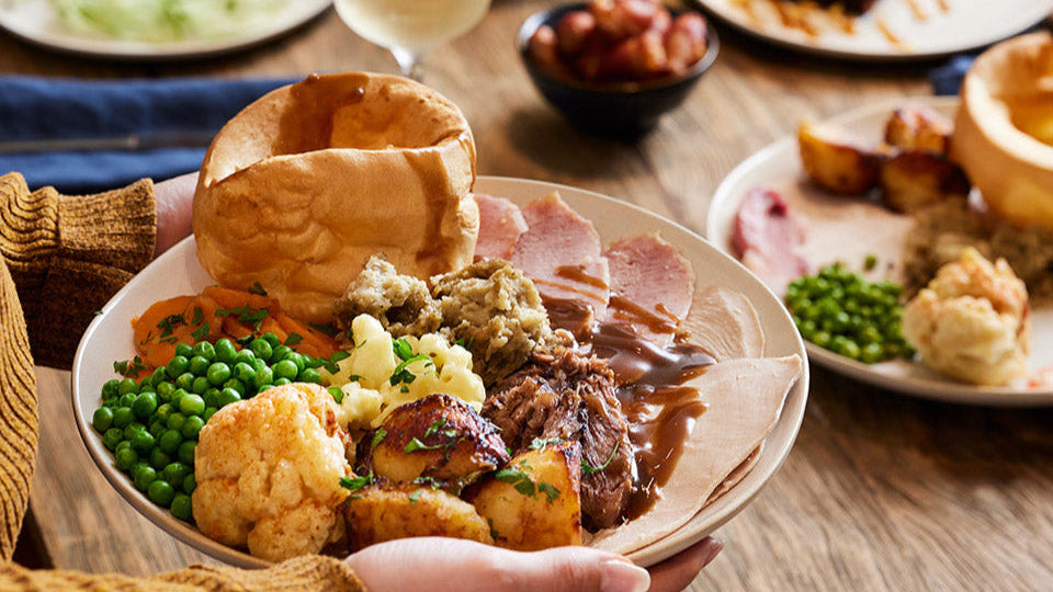 Plated meal with roast beef, vegetables, and Yorkshire pudding on a wooden table.