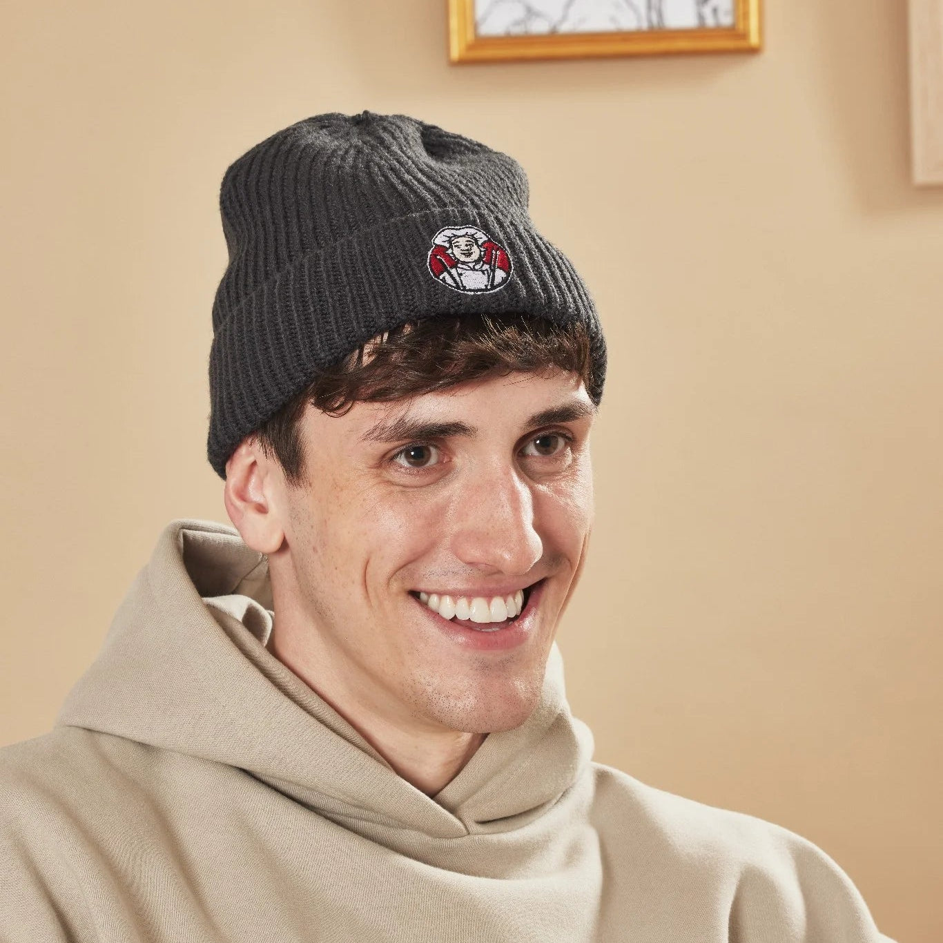Man wearing a graphite beanie with a Toby Carvery logo, smiling indoors.