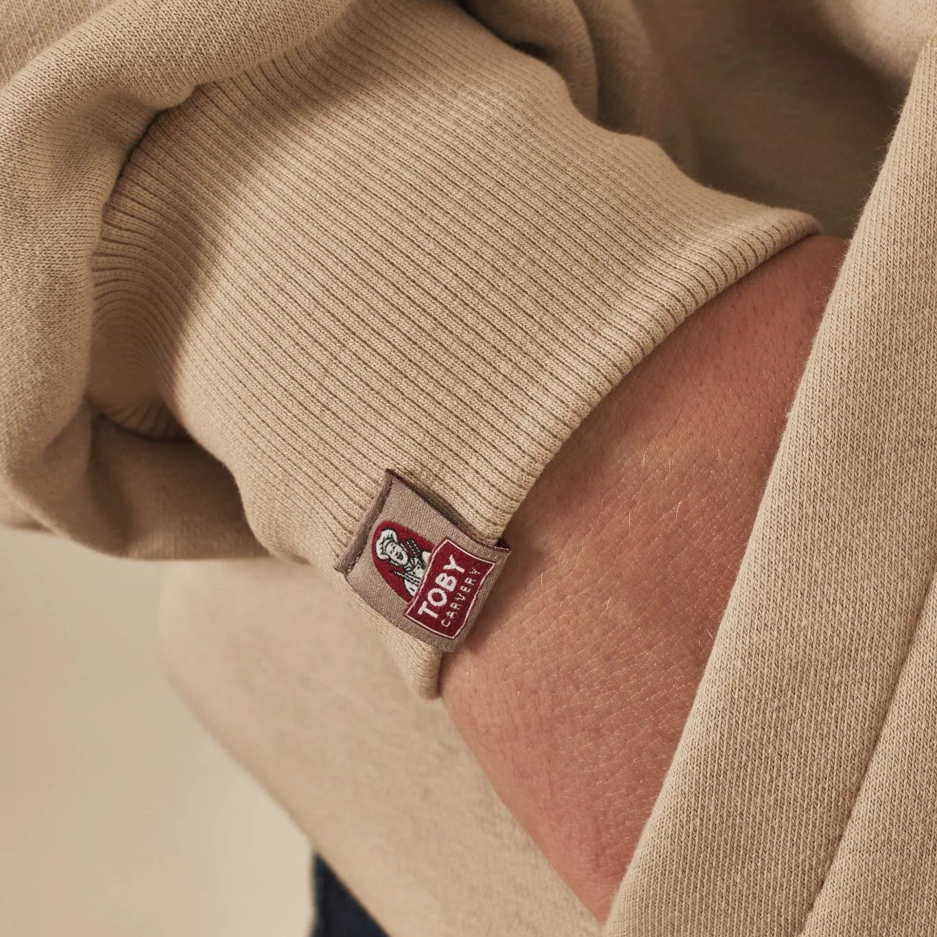 Close-up of a natural stone hoodie with a Toby Carvery label on a neutral background