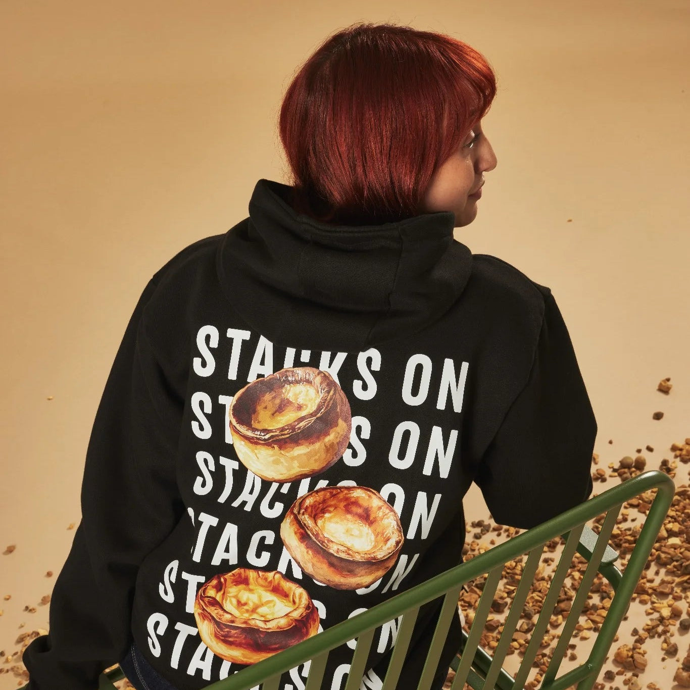 Person wearing a black hoodie with Yorkshire pudding design and text on the back, standing in front of a beige background.