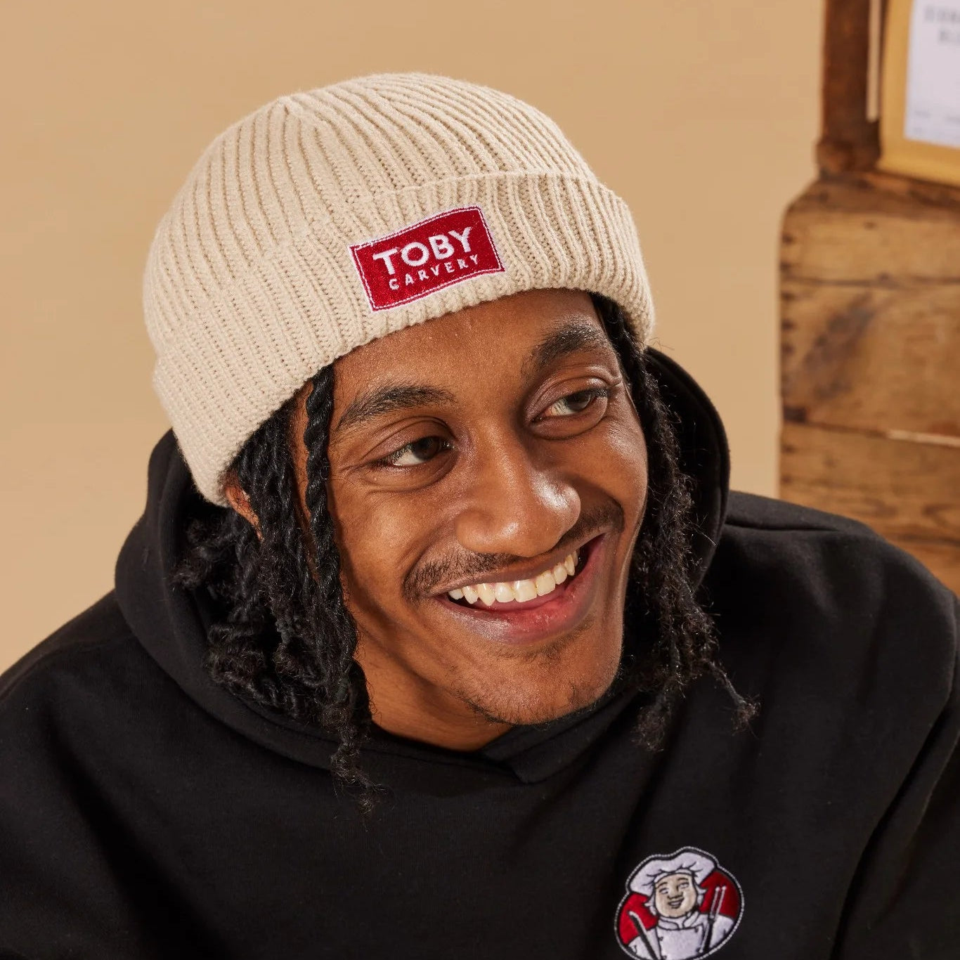 Person wearing an oatmeal knit beanie with 'Toby Carvery' logo and black hoodie with a Toby Carvery logo.