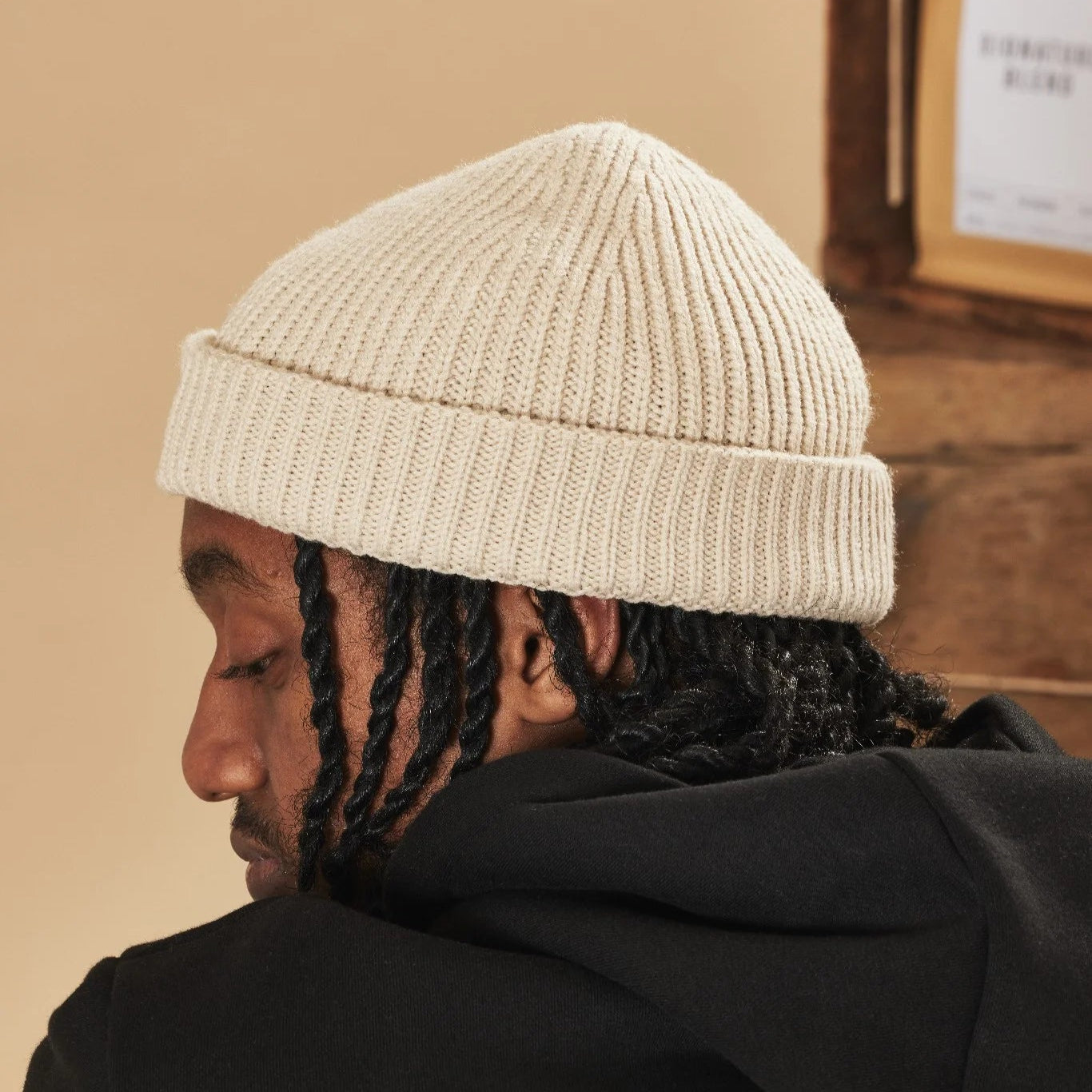 Person wearing an oatmeal beanie and black hoodie, sitting indoors.