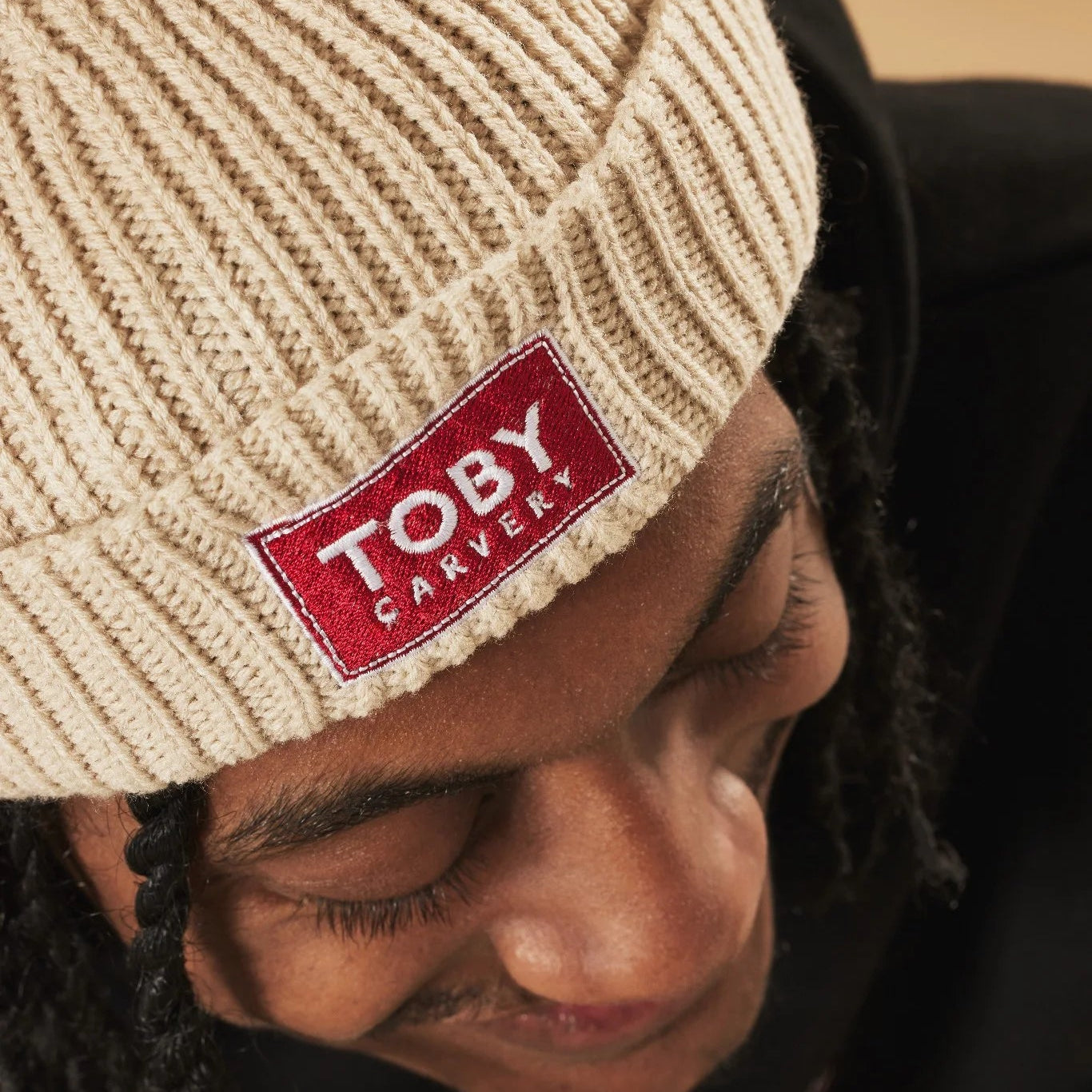 Person wearing an oatmeal knit beanie with a red 'Toby Carvery' logo.