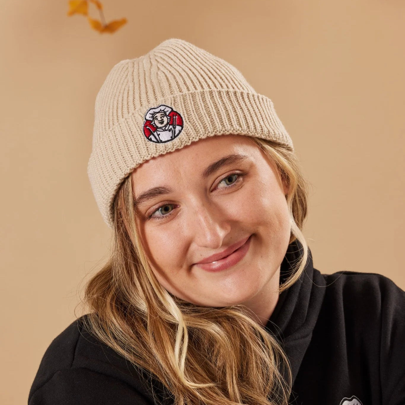 Person wearing an oatmeal beanie with a Toby Carvery logo on a beige background