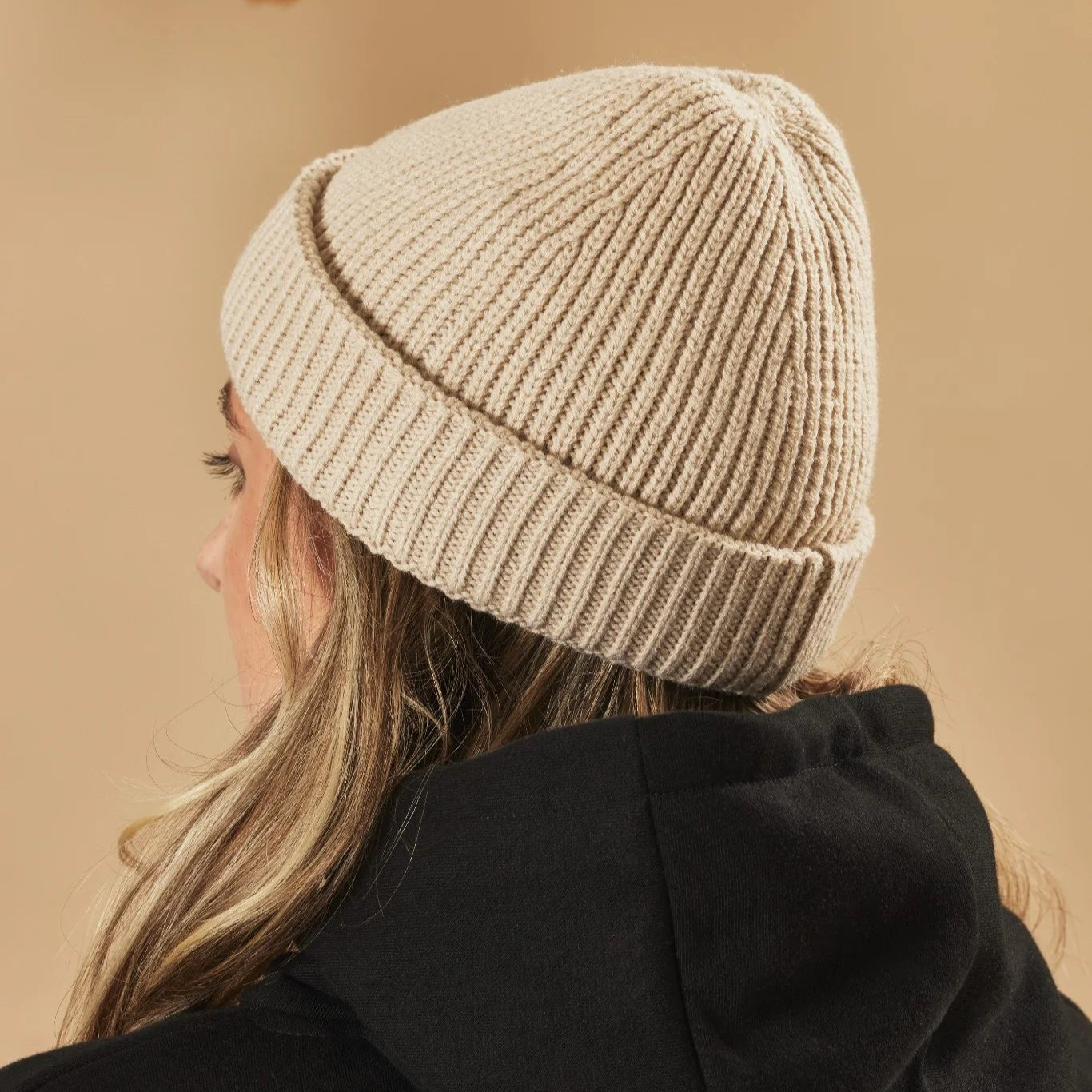 Oatmeal knit beanie worn by a person on a beige background