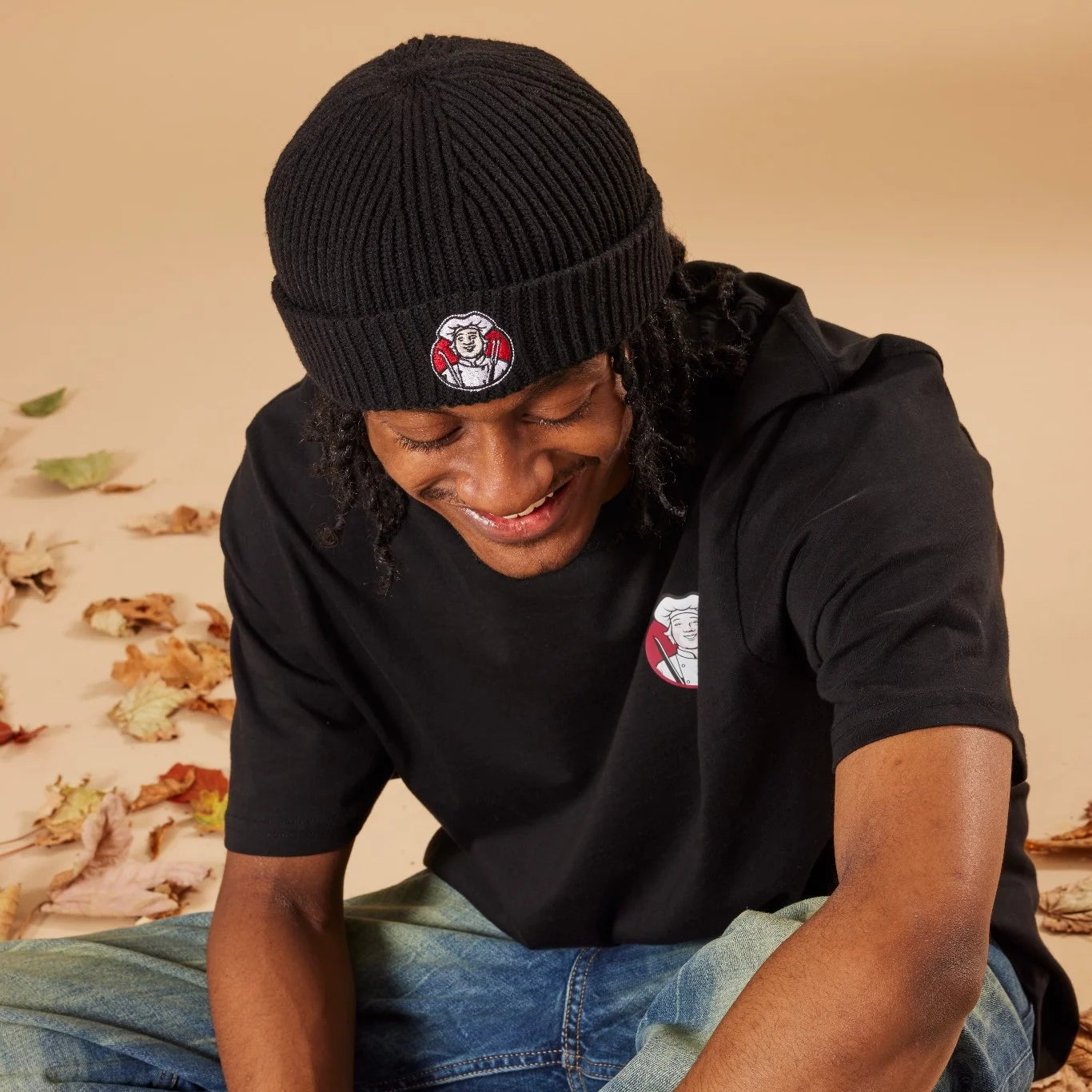 Person wearing a black beanie and black shirt with a Toby Carvery logo, sitting on a textured surface.