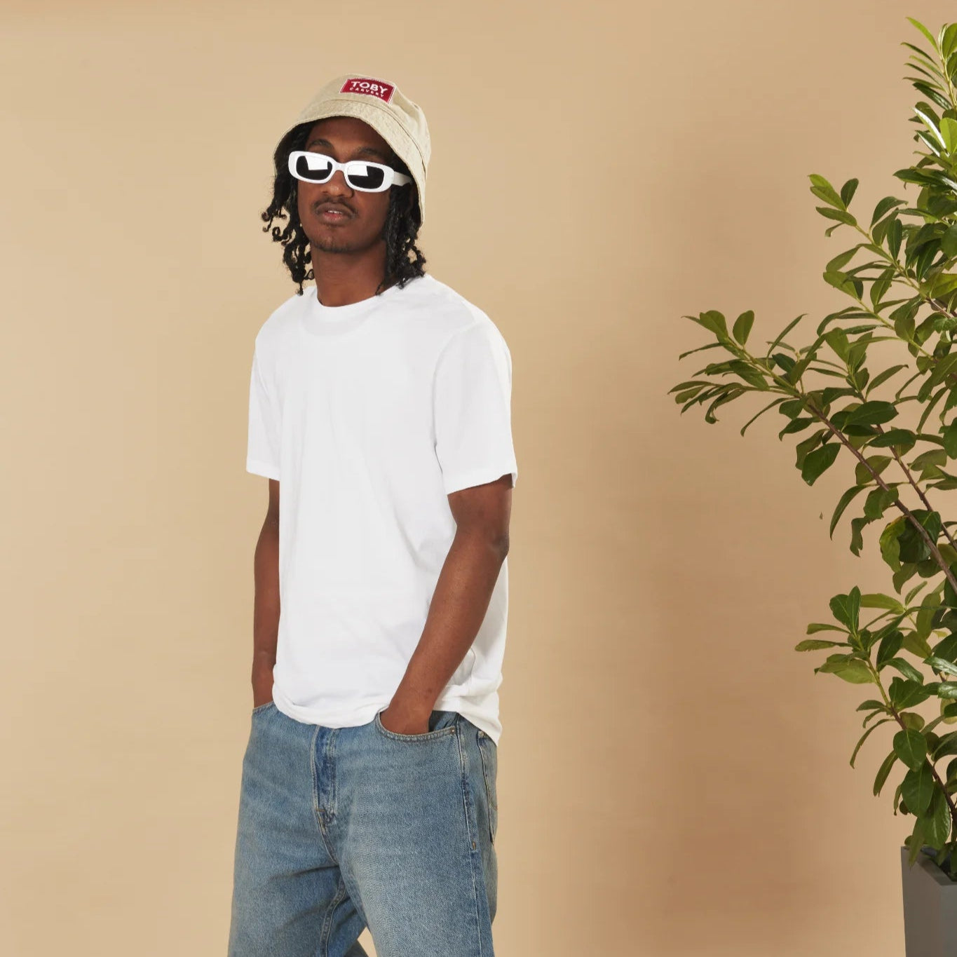 Person wearing a white t-shirt, blue jeans, and an oatmeal Toby Carvery bucket hat on a beige background