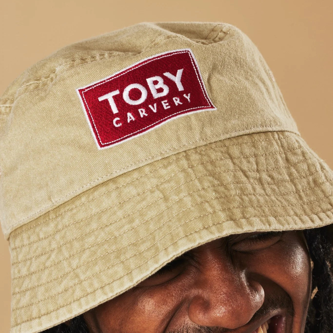 Oatmeal bucket hat with a red and white 'Toby Carvery' logo on a beige background
