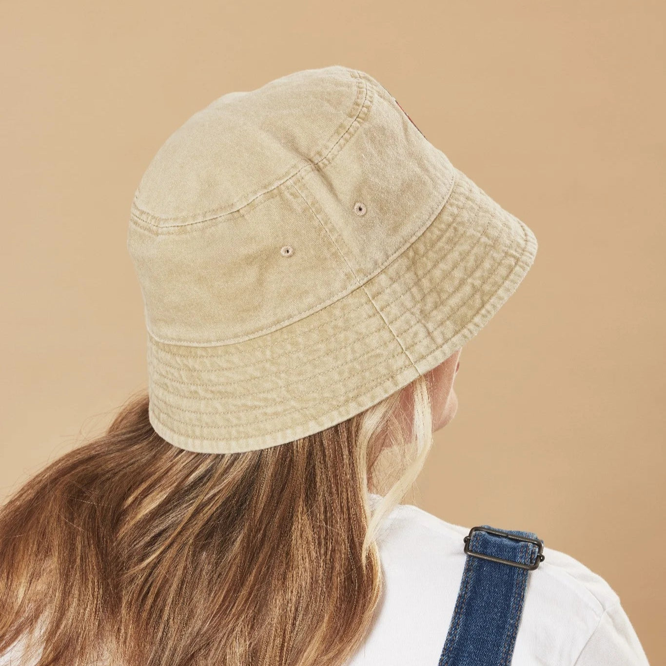 Person wearing an oatmeal bucket hat on a beige background