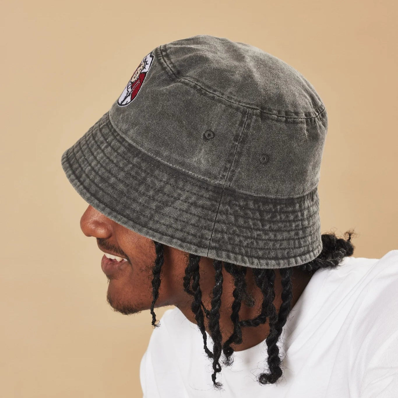 Person wearing a graphite bucket hat with a Toby Carvery logo on a beige background