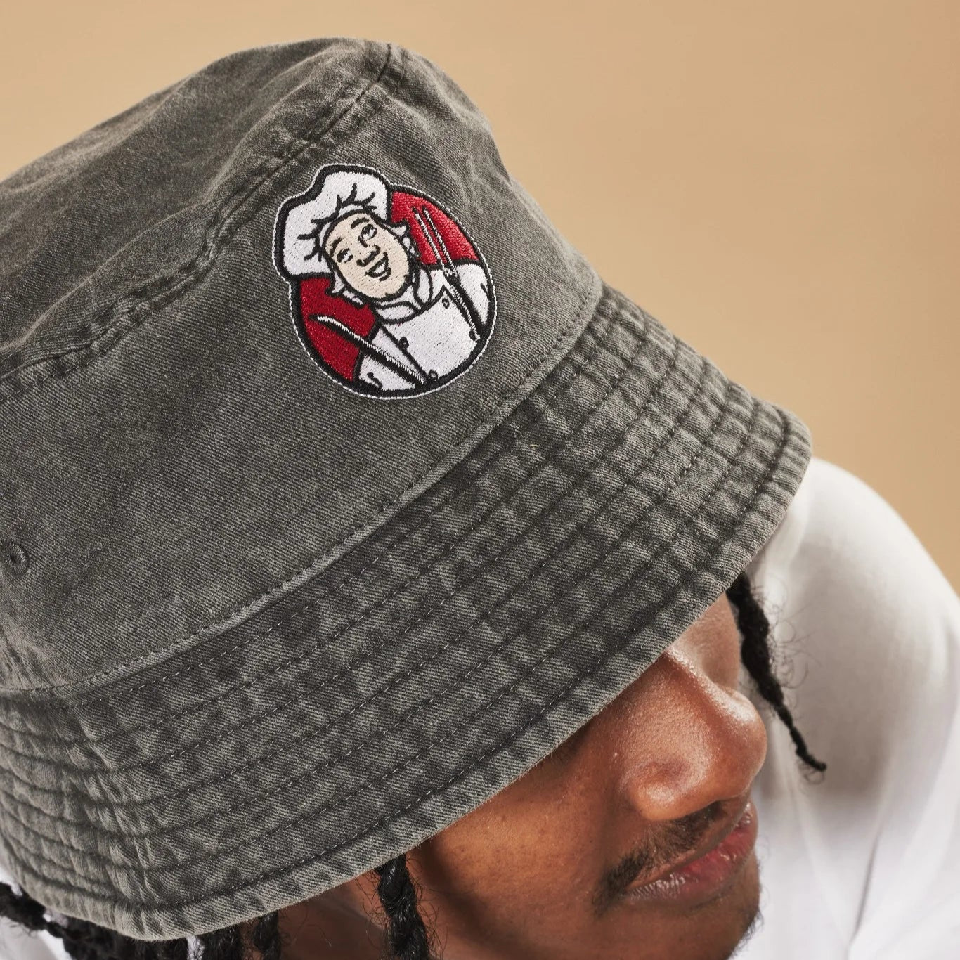 Graphite bucket hat with a Toby Carvery logo worn by a person against a beige background