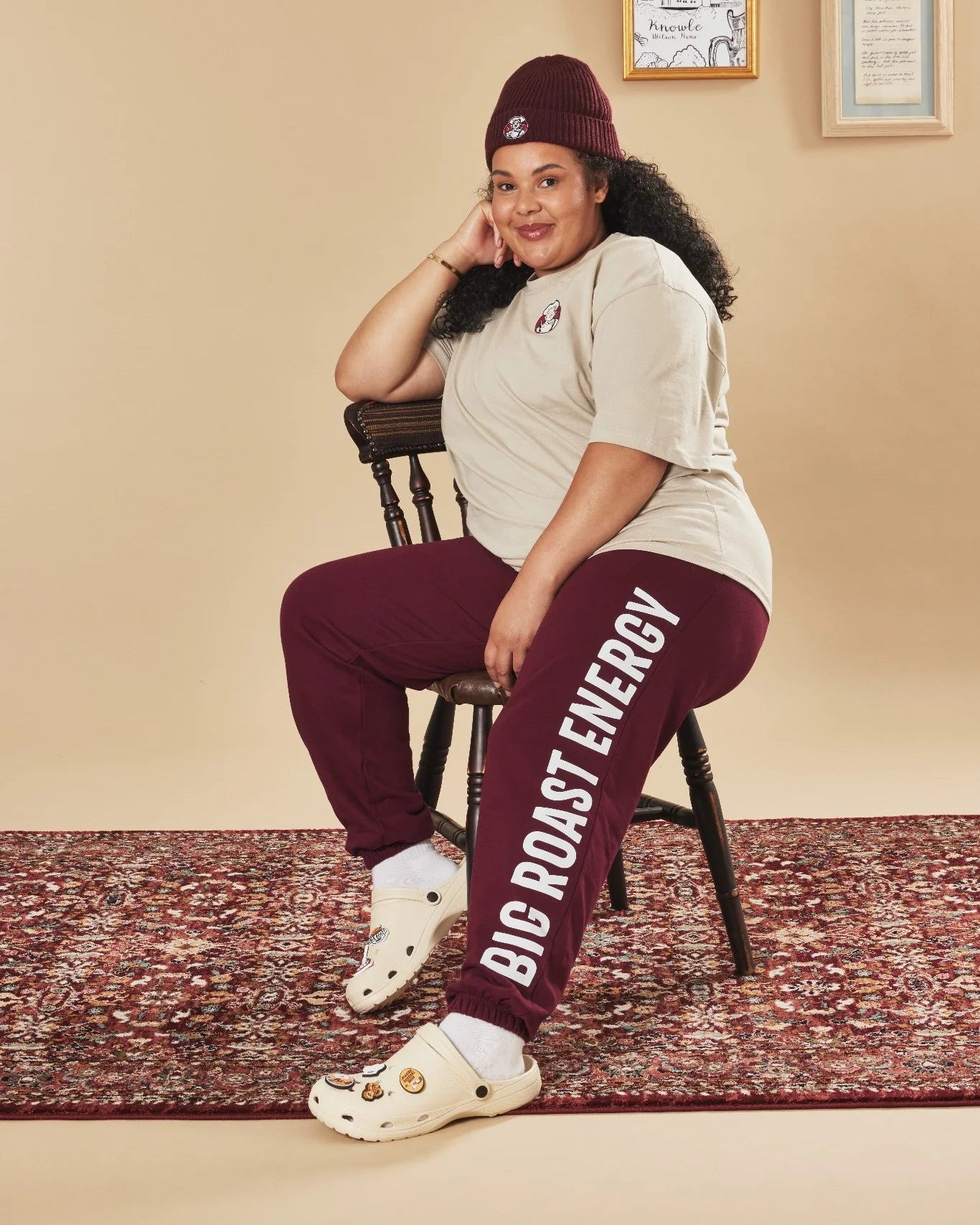 Person wearing burgundy and white sweatpants with text, sitting on a chair in a room.